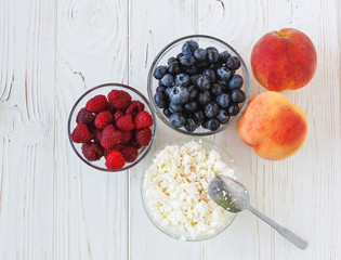 Healthy meal with organic cottage cheese, fresh raspberry, blueberry, peach on white wooden table. close up 