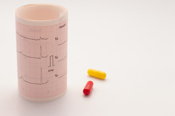 Electrocardiogram paper roll with the heart beat next to two colored pills. You can read the words Sync, v4, v5 and v6 and 10mm / Mv.