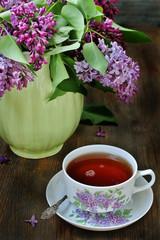Tea and a bouquet of lilac. Tea in a beautiful cup and a bouquet of lilac in a vase. A spring tea-party. Soft focus