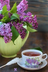 Tea and a bouquet of lilac. Tea in a beautiful cup and a bouquet of lilac in a vase. A spring tea-party. Soft focus
