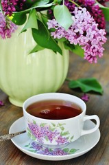 Tea and a bouquet of lilac. Tea in a beautiful cup and a bouquet of lilac in a vase. A spring tea-party. Soft focus