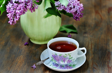 Tea and a bouquet of lilac. Tea in a beautiful cup and a bouquet of lilac in a vase. A spring tea-party. Soft focus