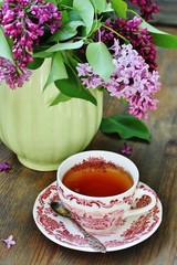 Tea and a bouquet of lilac. Tea in a beautiful cup and a bouquet of lilac in a vase. A spring tea-party. Soft focus
