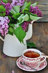 Tea and a bouquet of lilac. Tea in a beautiful cup and a bouquet of lilac in a vase. A spring tea-party. Soft focus