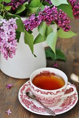 Tea and a bouquet of lilac. Tea in a beautiful cup and a bouquet of lilac in a vase. A spring tea-party. Soft focus