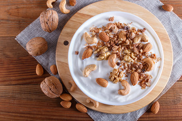 White plate with greek yogurt, granola, almond, cashew, walnuts  on brown wooden background.