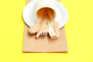 Eco-friendly disposable utensils made of bamboo wood on paper bag on yellow background.