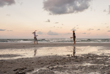 Fototapeta na wymiar Coppia adulti gioca a racchette sulla spiaggia al mare al tramonto