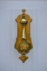 Llamador de puerta dorado sobre puerta blanca.