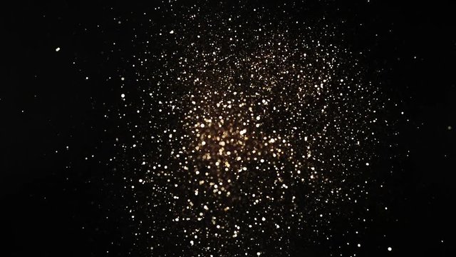 Golden glitter explosion in super slow motion on black background.