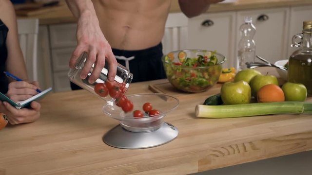 Male hands throwing cherry tomatoes on electronic scales for weighing making a new recipe for cooking dietary salad. Healthy food