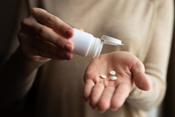 Female hand holds medicine, woman hands with pills pills from a bottle. Pain, home treatment. Dark picture