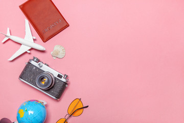 Vacation travel summer weekend sea adventure trip concept. Minimal simple flat lay with plane vintage camera passport sunglasses globe piggy bank and shell on pink pastel trendy modern background