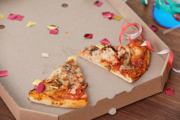 Pizza box with leftovers and confetti on table, closeup. After party chaos