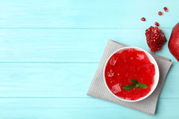 Flat lay composition with red jelly in bowl and pomegranate on wooden background. Space for text