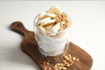 Glass of tasty chia seed pudding with banana and granola served on table