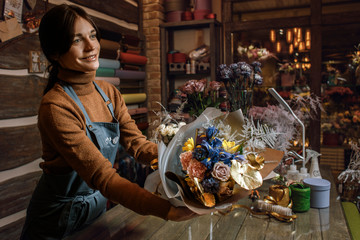 Happy woman gardener in the flower shop make bouquets for a holiday. Flower's business. Lifestyle flower shop. Girl create a beautiful flower composition for sale.
