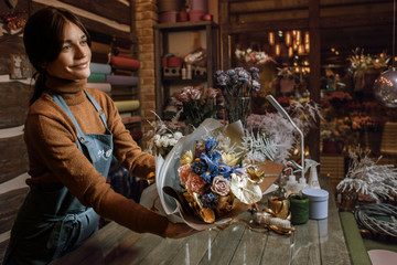 Happy woman gardener in the flower shop make bouquets for a holiday. Flower's business. Lifestyle flower shop. Girl create a beautiful flower composition for sale.