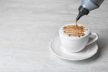 Adding caramel topping to latte macchiato on table, space for text