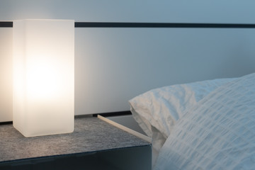 Modern square lamp on a nightstand lighting up a dark bedroom