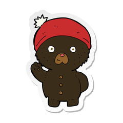 sticker of a cartoon waving black teddy bear in winter hat