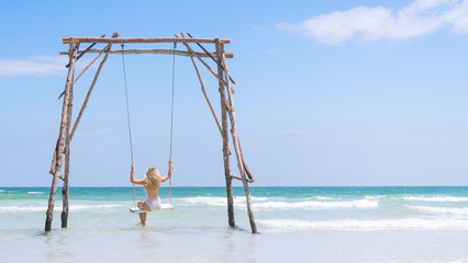 Beautiful Young Blonde Traveler Girl in a white swim suit, Swinging on a Sea Swing Framed off to the left in Phu Quoc Island, Vietnam