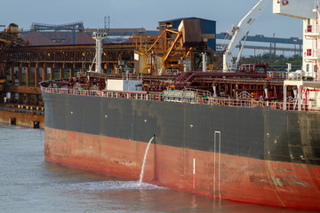 Tanker discharging cooling water water in harbor waters at evening time