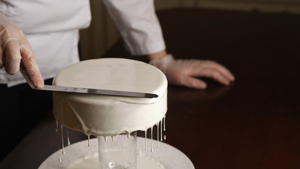 Confectioner fills cakes with white liquid glaze. She equals top surface of cake. Excess cream drains from baking.