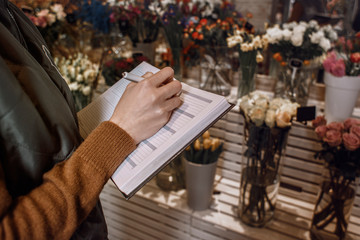 Girl writes in a notebook about a flower's shop. Management. Business writing. Woman hands write to the notebook about the flowers. Detail. Close up.