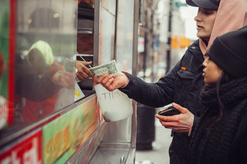 People buy street food in New York City and pay in cash to the seller