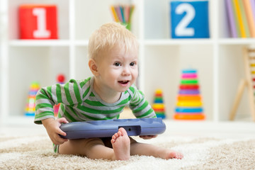 Funny toddler sitting on carpet with musical toy in nursery