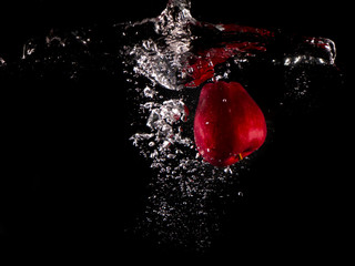 red apple , yellow lemon falling into splashing water on black background