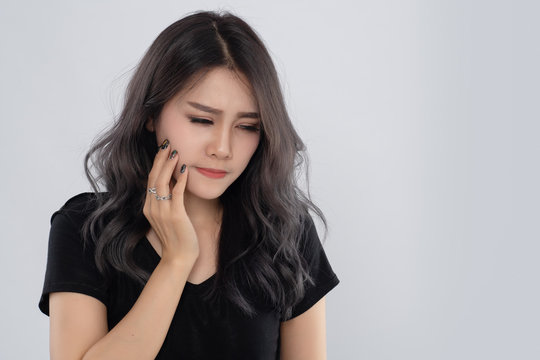 Asian  woman holds for face feeling painful toothache. Dental care and health concept. Beautiful young female suffering from toothache on grey background.