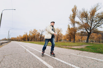 Fototapeta premium The original pensioner goes on rollers in the autumn park. Happy pension. Active old people.
