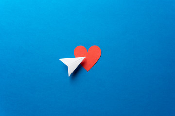 Paper plane with red heart shape on blue background. Sharing and send concept.