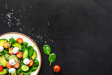 Fresh salad with mozzarella, spinach, cherry tomatoes, cucumber on plate on black background top view space for text