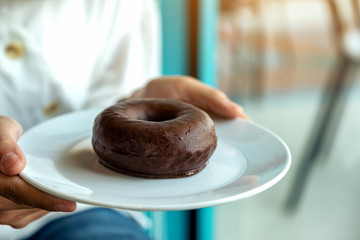 A woman holding and showing a plate of chocolate donut