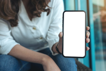 Mockup image of a woman holding and showing black mobile phone with blank white screen in cafe