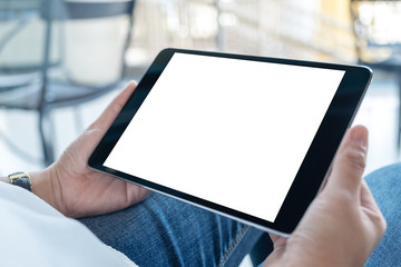 Fototapeta premium Mockup image of a woman holding black tablet pc with blank white screen horizontally while sitting in cafe