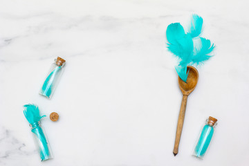 Frame formed of small bottles. Composition of turquoise feathers and spoons. Marble surface. Flat lay, top view