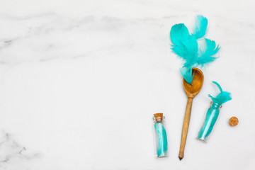 Composition of turquoise feathers and a wooden spoon on a marble surface. Two beautiful little bottles. Flat lay, top view, copy space