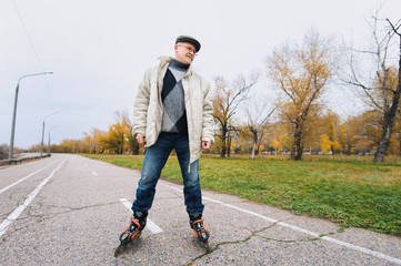 Fototapeta premium The original pensioner goes on rollers in the autumn park. Happy pension. Active old people.