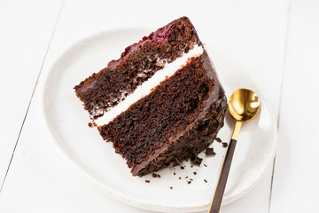Slice of chocolate cake with cream frosting on white plate and golden tea spoon for eating. Closeup view