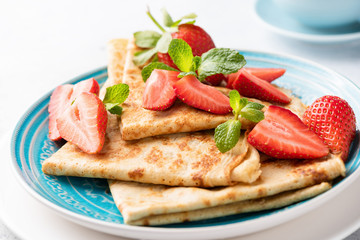 Blini or crepes with strawberry on a blue plate, closeup view. Tasty thin pancakes for breakfast or dessert served with fresh red berries