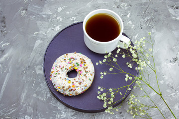 top view cofee mug, donut on a plat and flowers on a conrete background