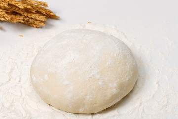 Raw fresh dough in the flour and ears of wheat on a white background