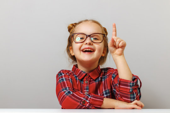 Back to school. Funny little girl with glasses points finger up. Education concept. Gray background