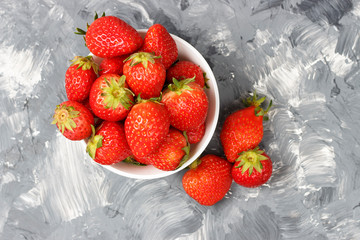 Strawberries in a white bowl on a gray background, top view