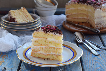 A piece of delicious coconut layer cake - a biscuit and cream on coconut cream, decorated with grated chocolate and candied rose petals.