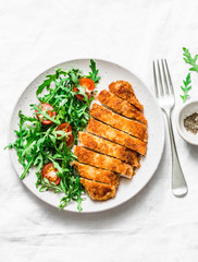 Traditional chicken schnitzel with arugula cherry tomatoes salad on light background, top view